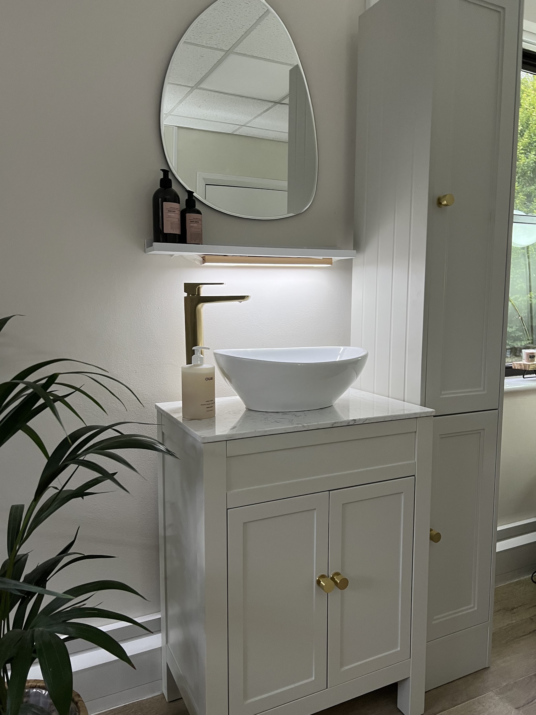 The studio's basin with a gold tap, round mirror and a trailing plant