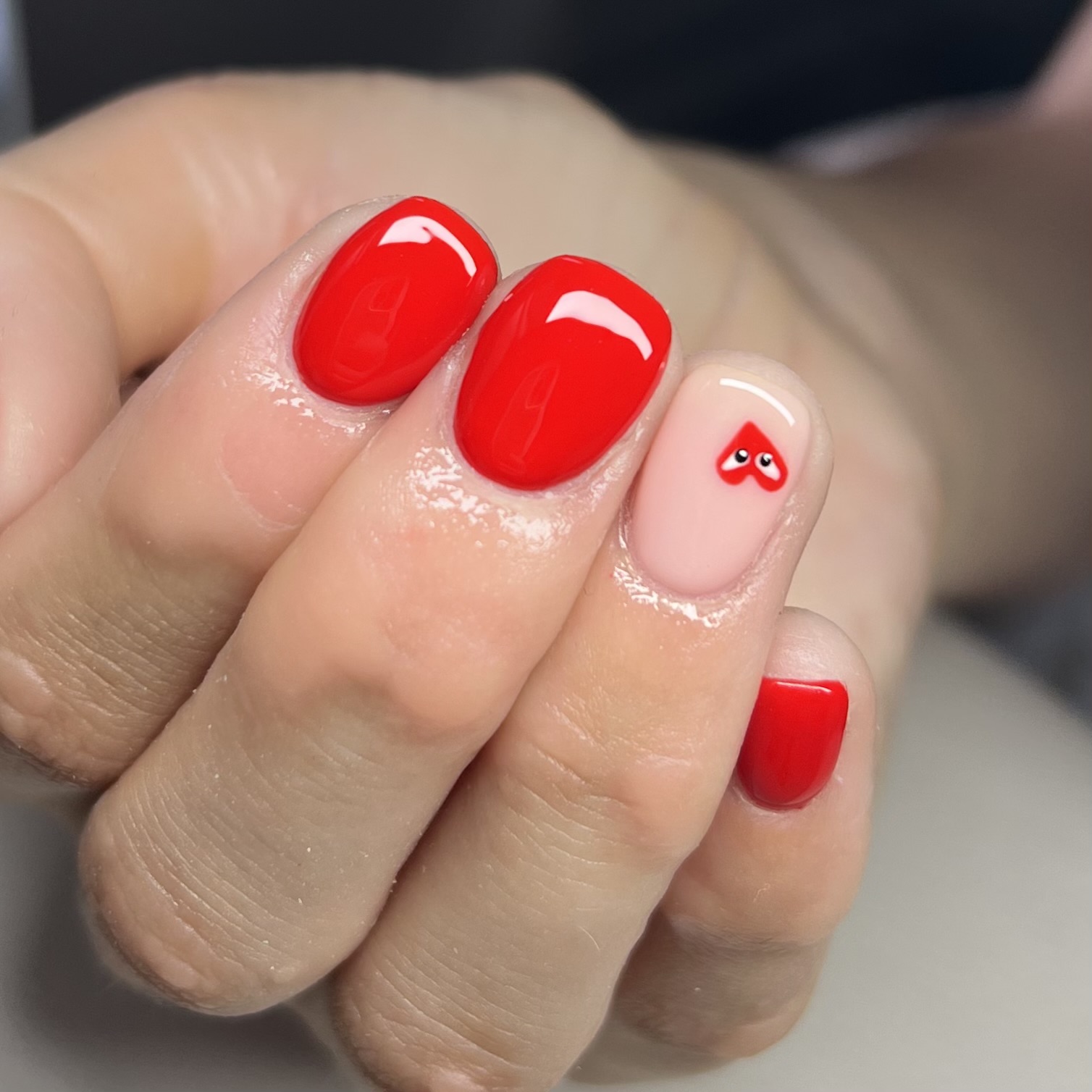 Red gel nails with a little heart on a nude accent nail