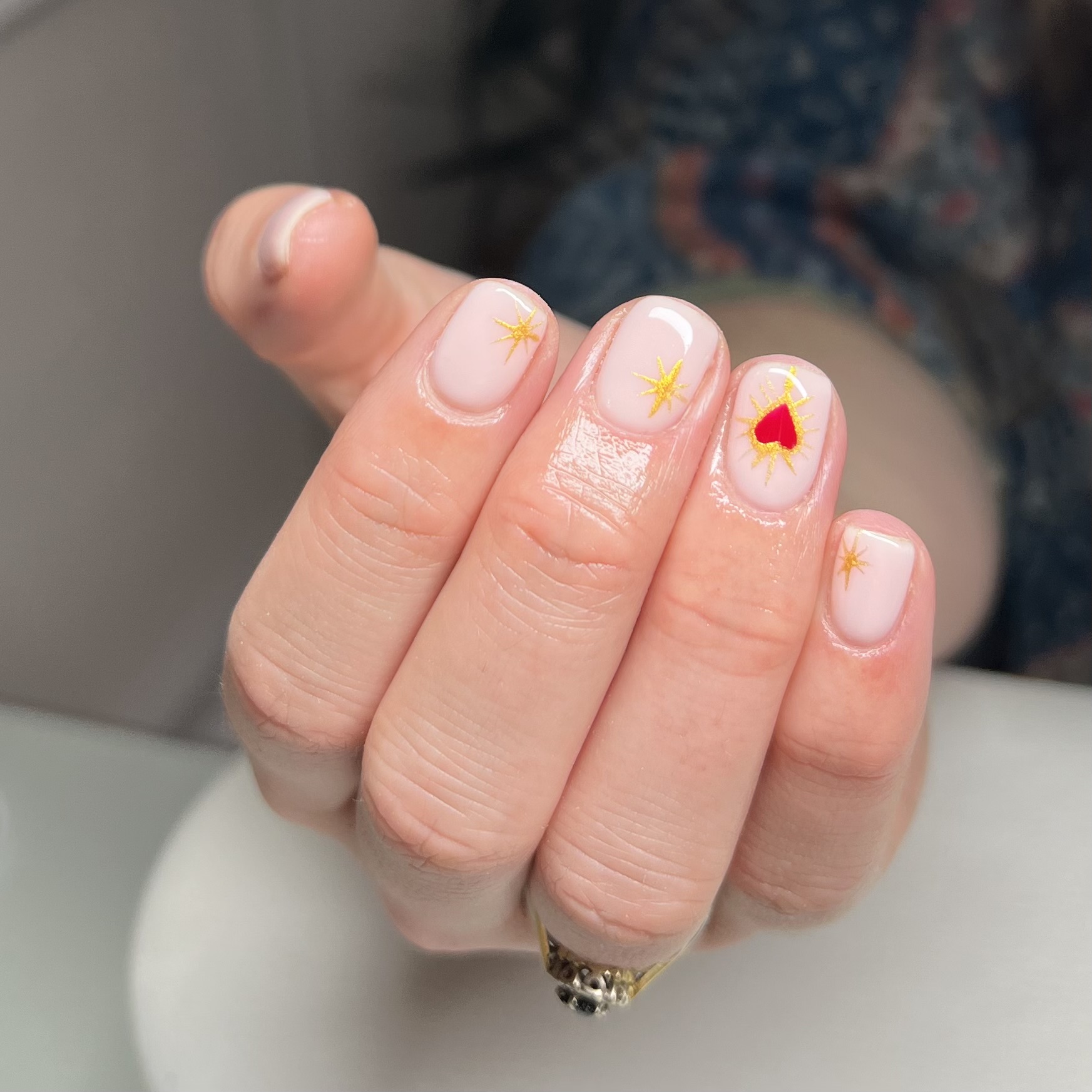 Nude BIAB nails with tiny gold sparkles and a red heart